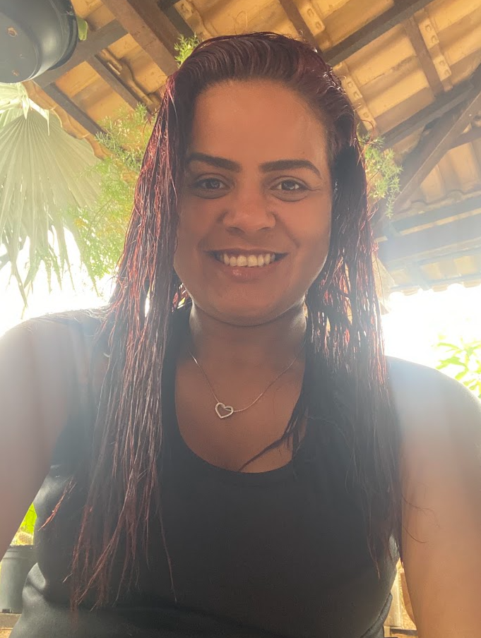 Mulher sorrindo para a câmera, com cabelos longos avermelhados e usando uma blusa preta.
